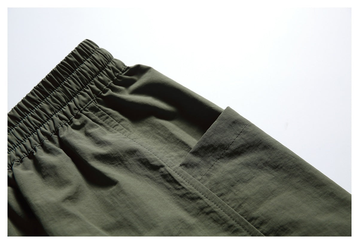 Close-up of dark olive shorts showing the gathered elastic waistband, stitching, and a large patch pocket.