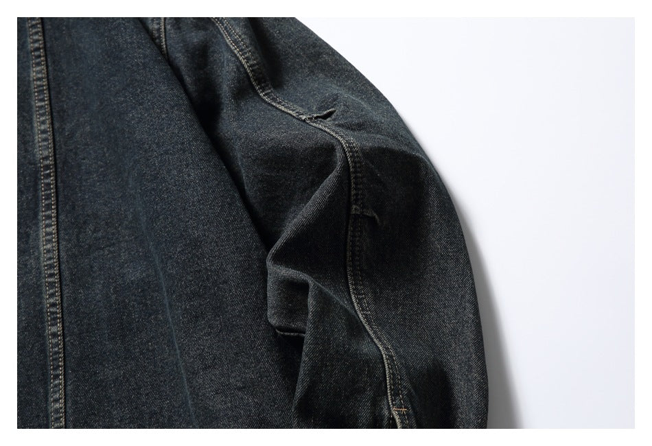 Close-up of dark indigo denim with tan topstitching and a folded seam against a white background.