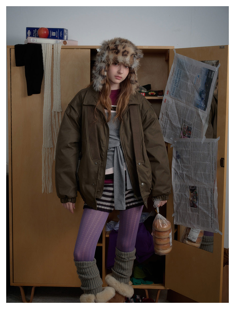 Front view of a model in an oversized olive-brown jacket with ribbed panels, styled with a spotted faux-fur hat.