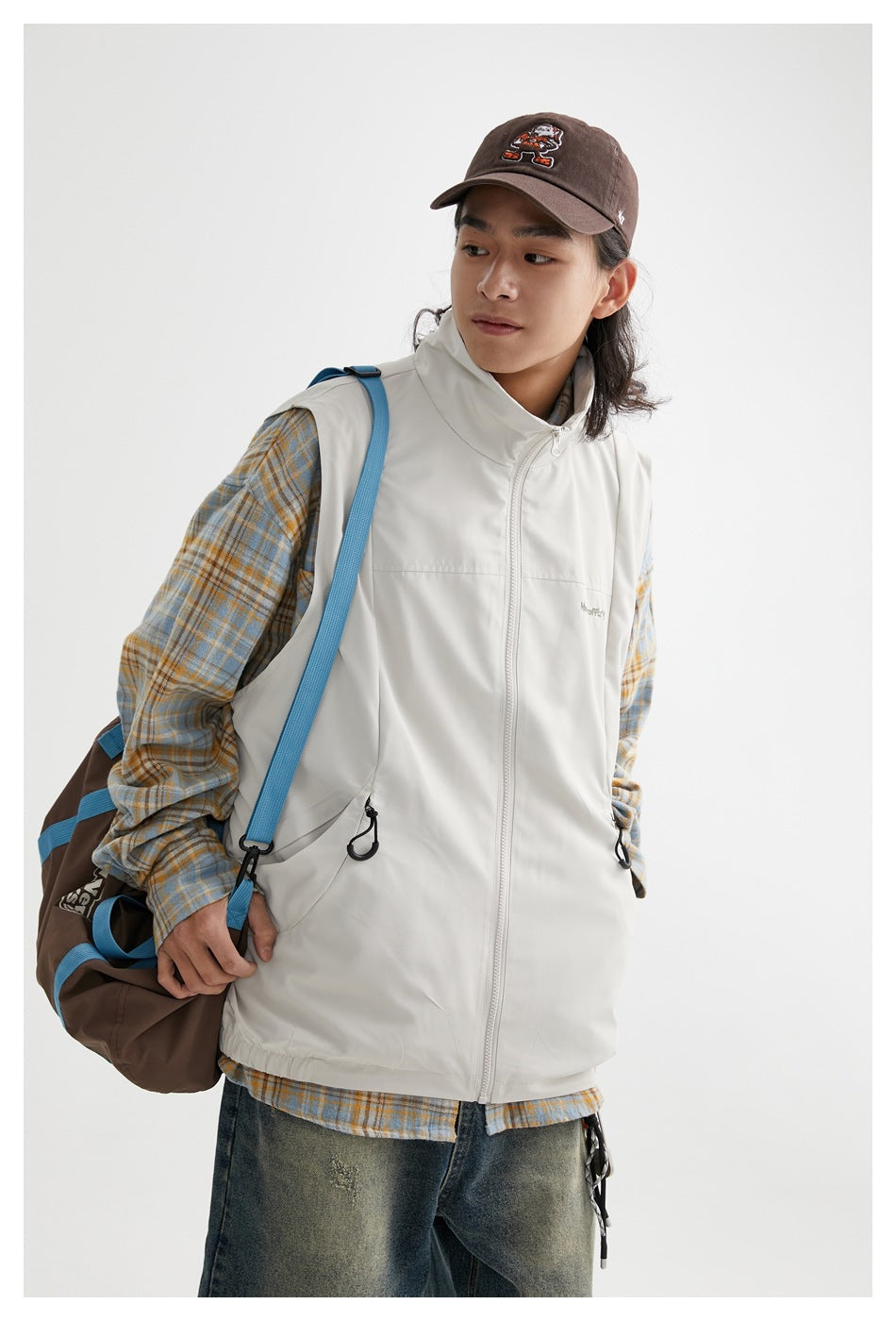 Closer front view of a model wearing an off-white high-collar zip vest with drawcord pockets over a plaid shirt.