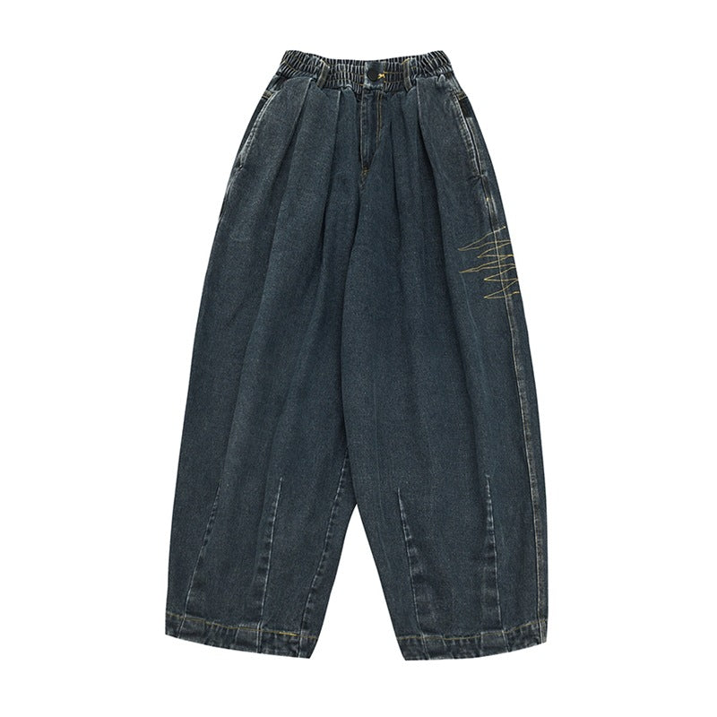 Front flat-lay of blue washed denim barrel-leg jeans with front pleats and gold zigzag embroidery on the side