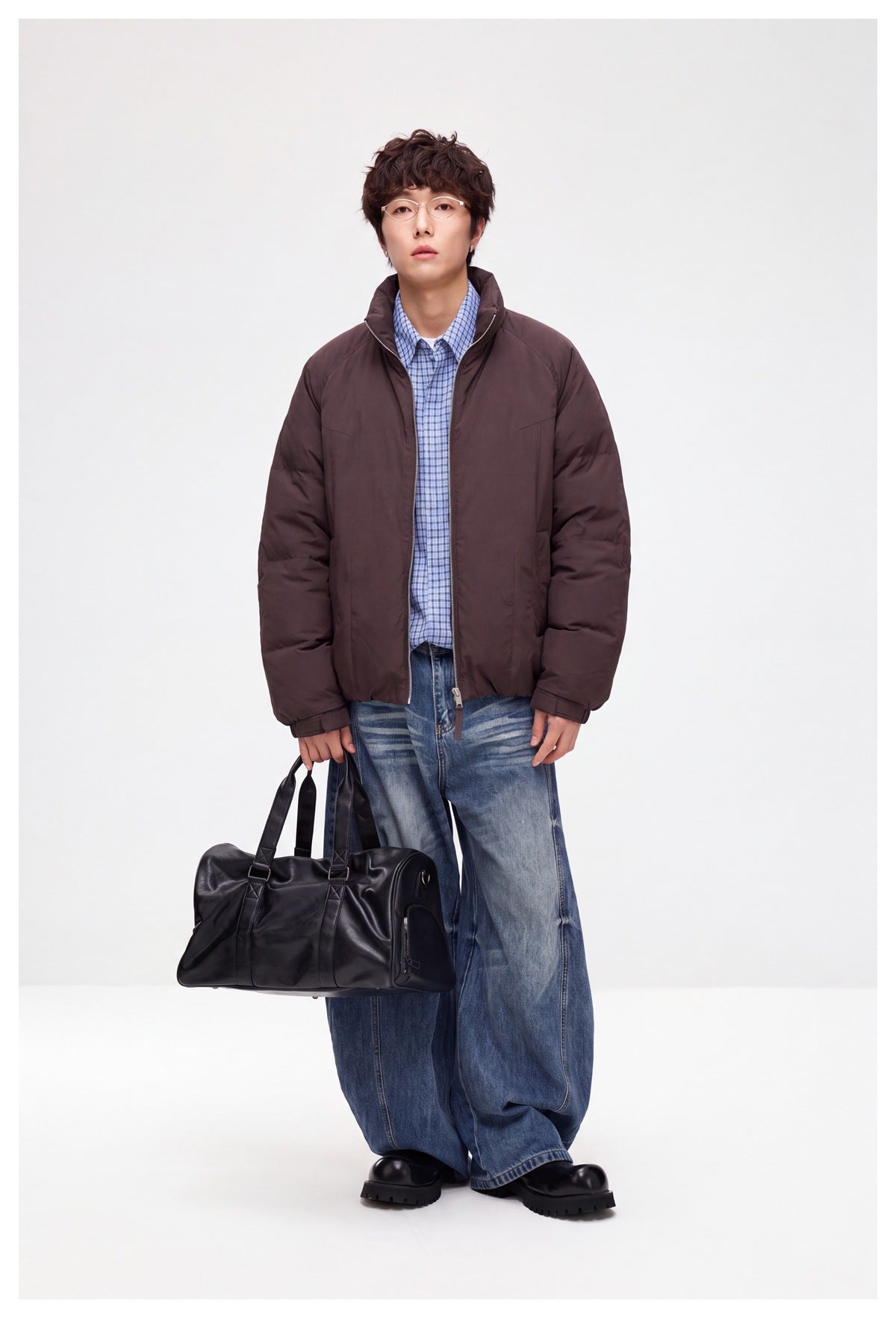 Full-length model wearing an open dark brown padded jacket with a raised collar, paired with jeans and carrying a black bag.
