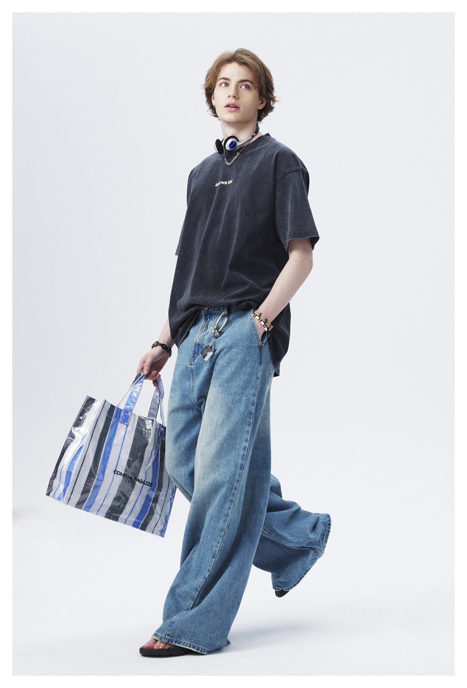 Model walking in a dark oversized T-shirt and wide-leg blue jeans, carrying a blue-and-white striped tote.