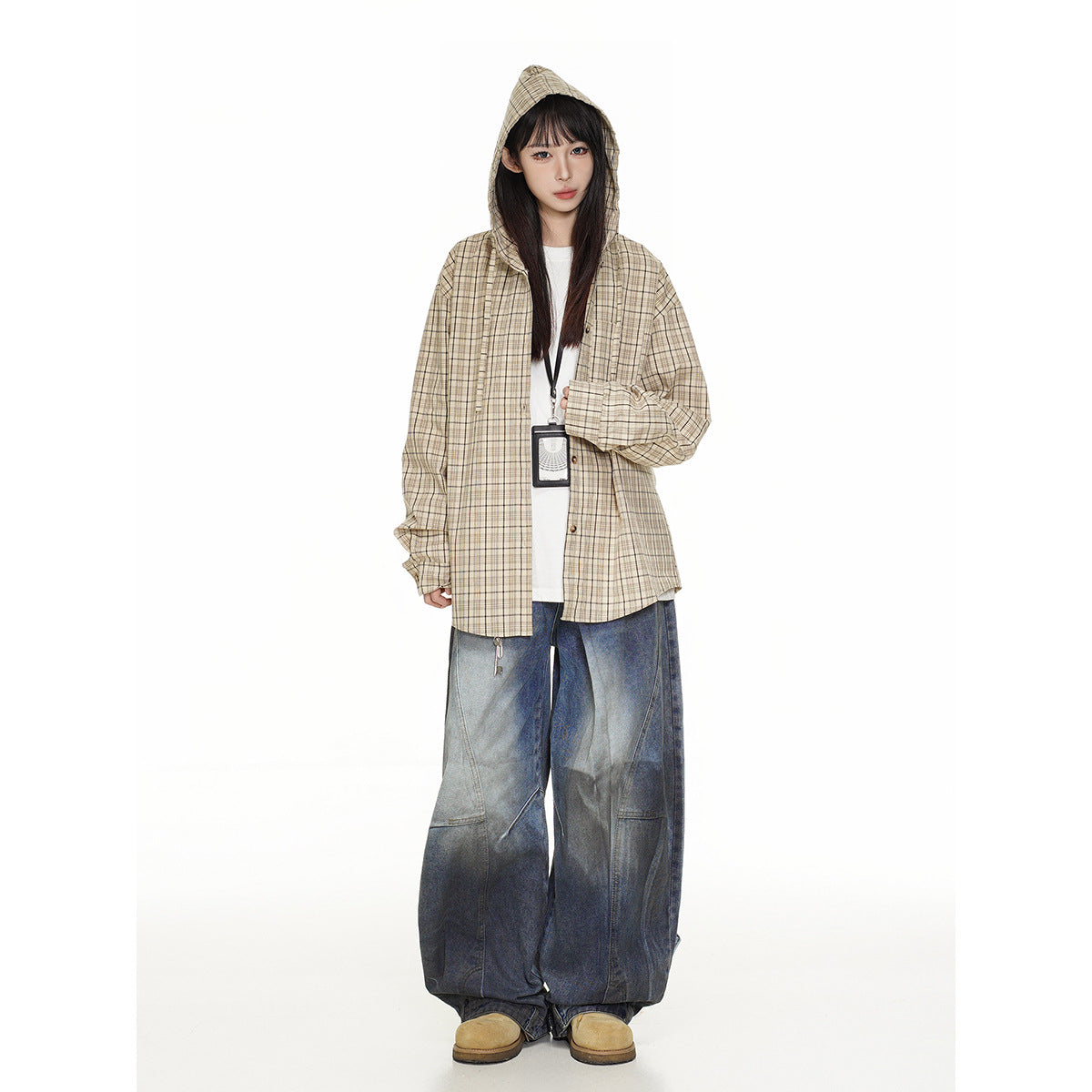 Front view of a model wearing a beige plaid hooded overshirt, white top, and very wide blue jeans.