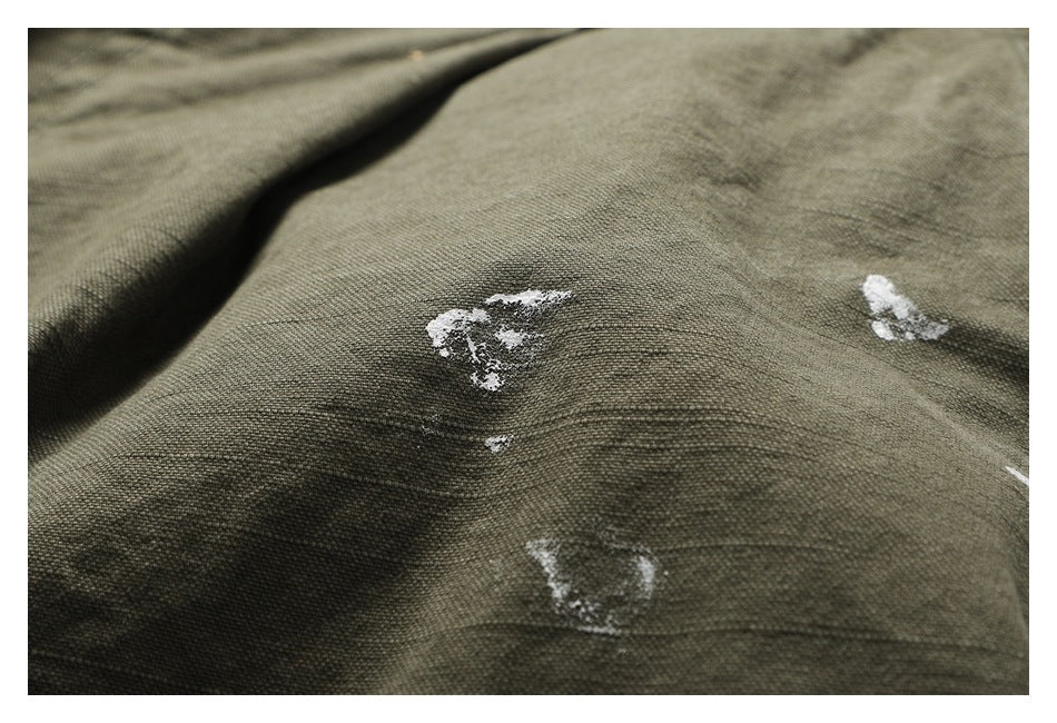 Close-up of olive trouser fabric with scattered pale distressed marks.