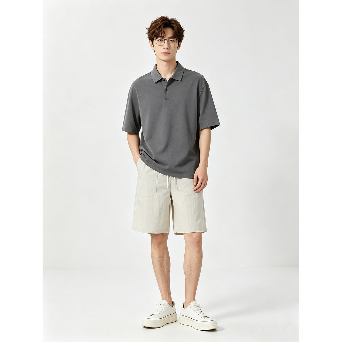Model wearing a charcoal gray polo shirt, cream shorts, and white sneakers.