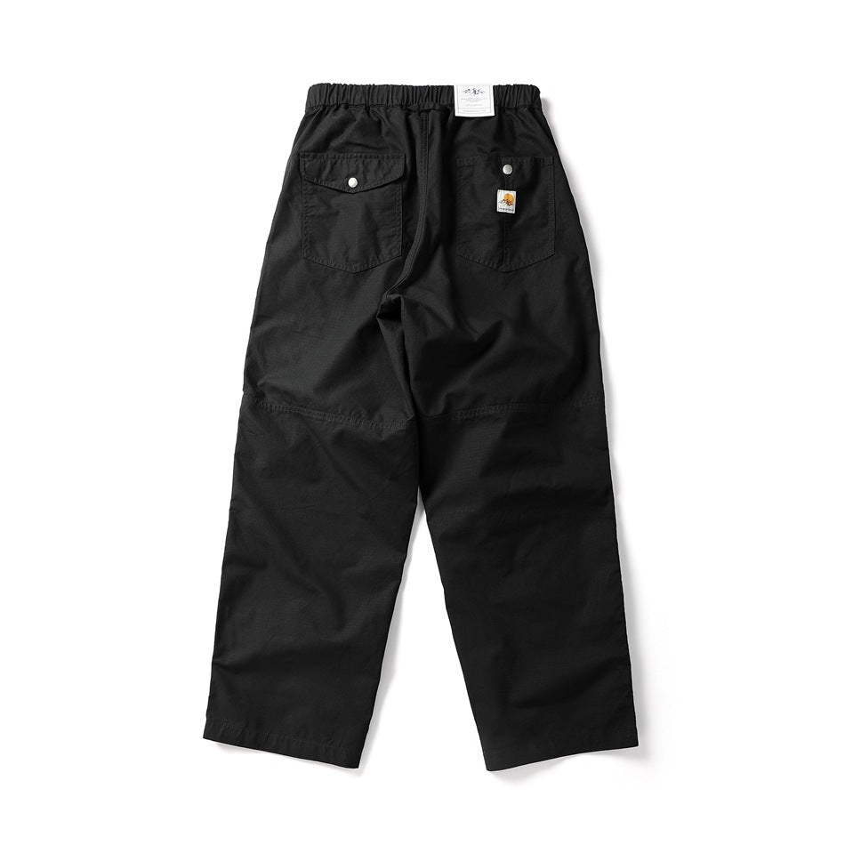 Flat-lay back of black wide-leg pants with a snap-flap pocket, a patch pocket, a knee seam and an elastic waist