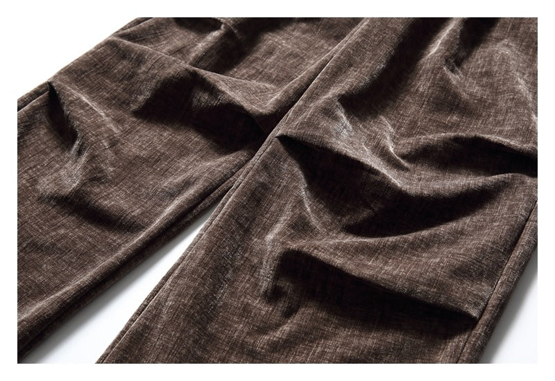 Close-up of brown textured trouser legs highlighting the front pleats and stitching.