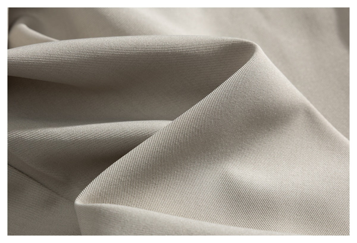 Close-up of light beige fabric draped in folds, showing its fine diagonal weave.