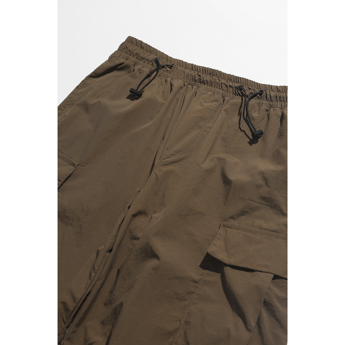 Close-up of brown cargo pants showing an elastic drawcord waist, front pocket, and flap cargo pocket.