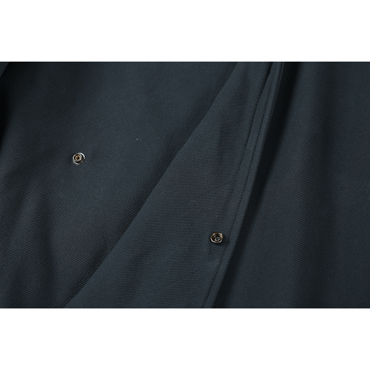 Close-up of the dark charcoal jacket's overlapping front placket with two metal snap fasteners.