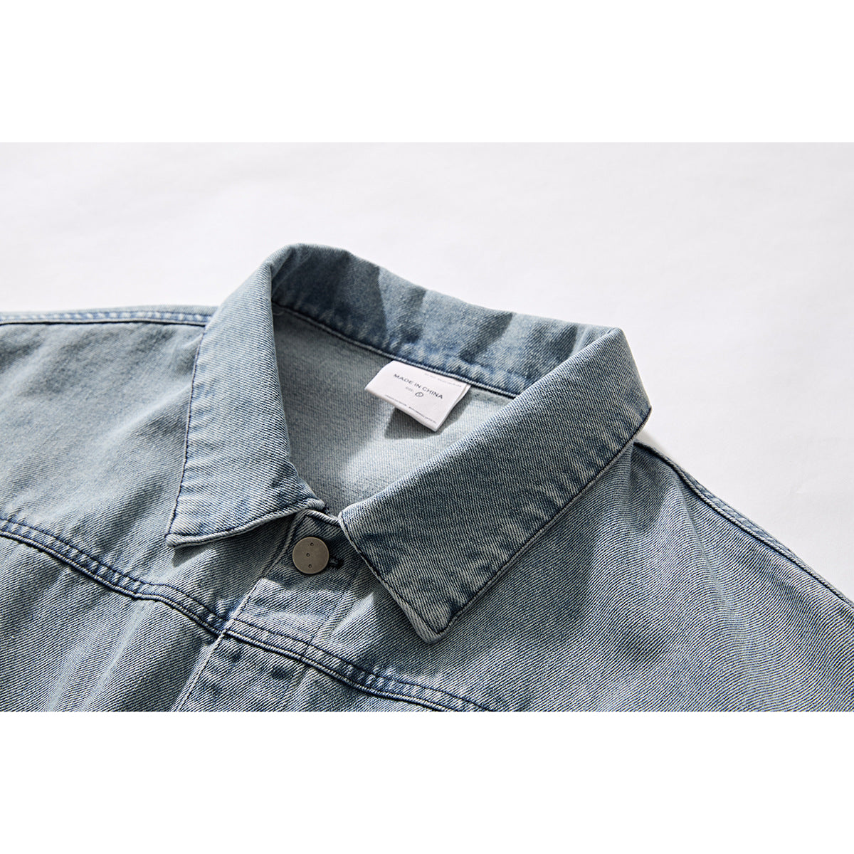 Close-up of a light blue washed denim jacket collar, top button, seams, and inner neck label.