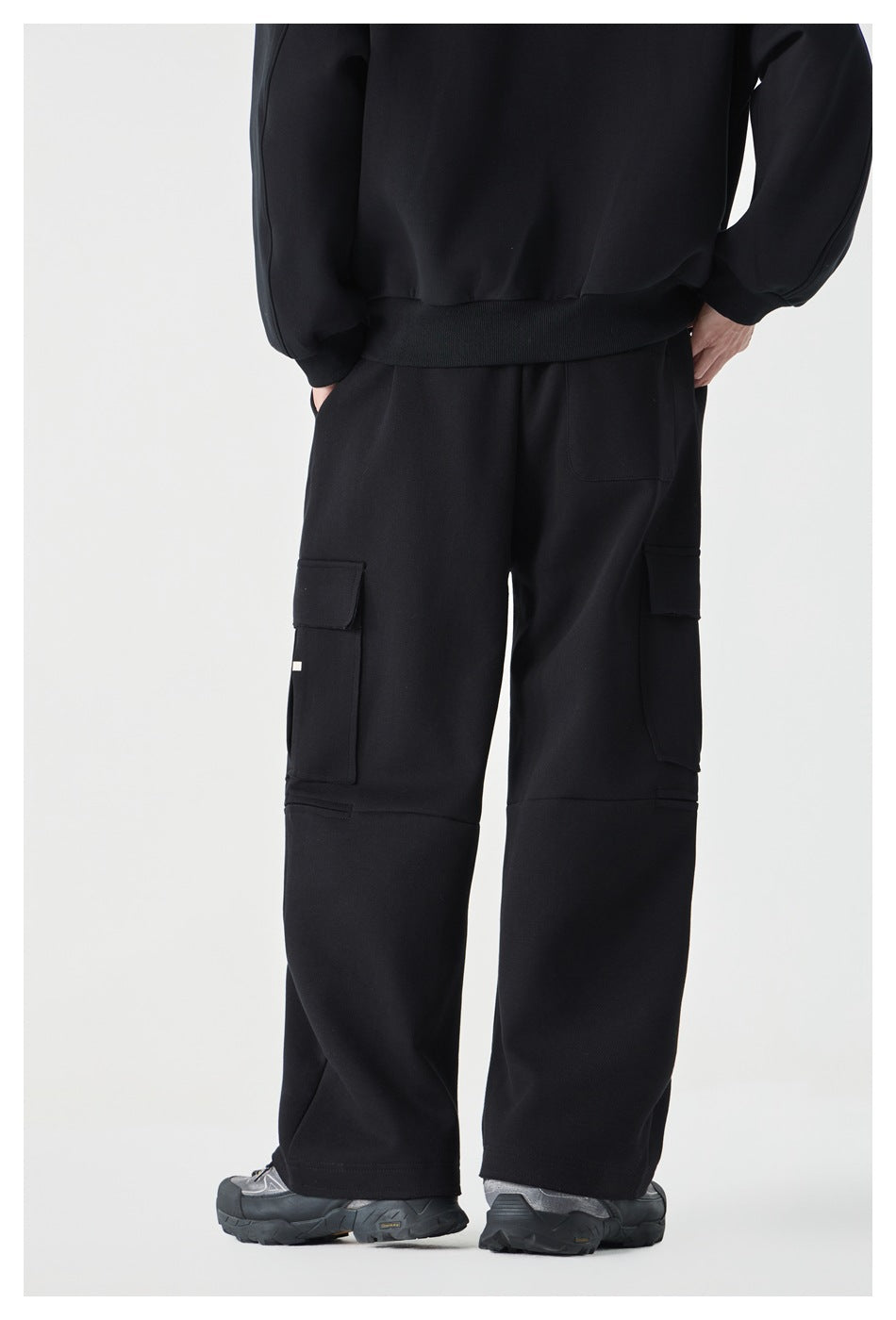 Rear view of a cropped model wearing black wide-leg cargo pants with flap pockets on both legs.