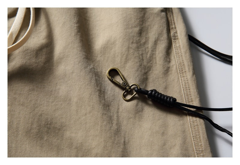 Close-up of a black cord with a metal clip against the khaki trouser fabric.