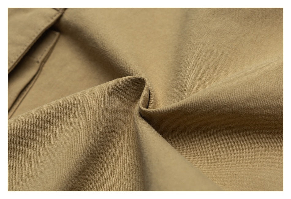 Close-up of tan garment fabric arranged in folds, with a stitched seam visible at the upper left.
