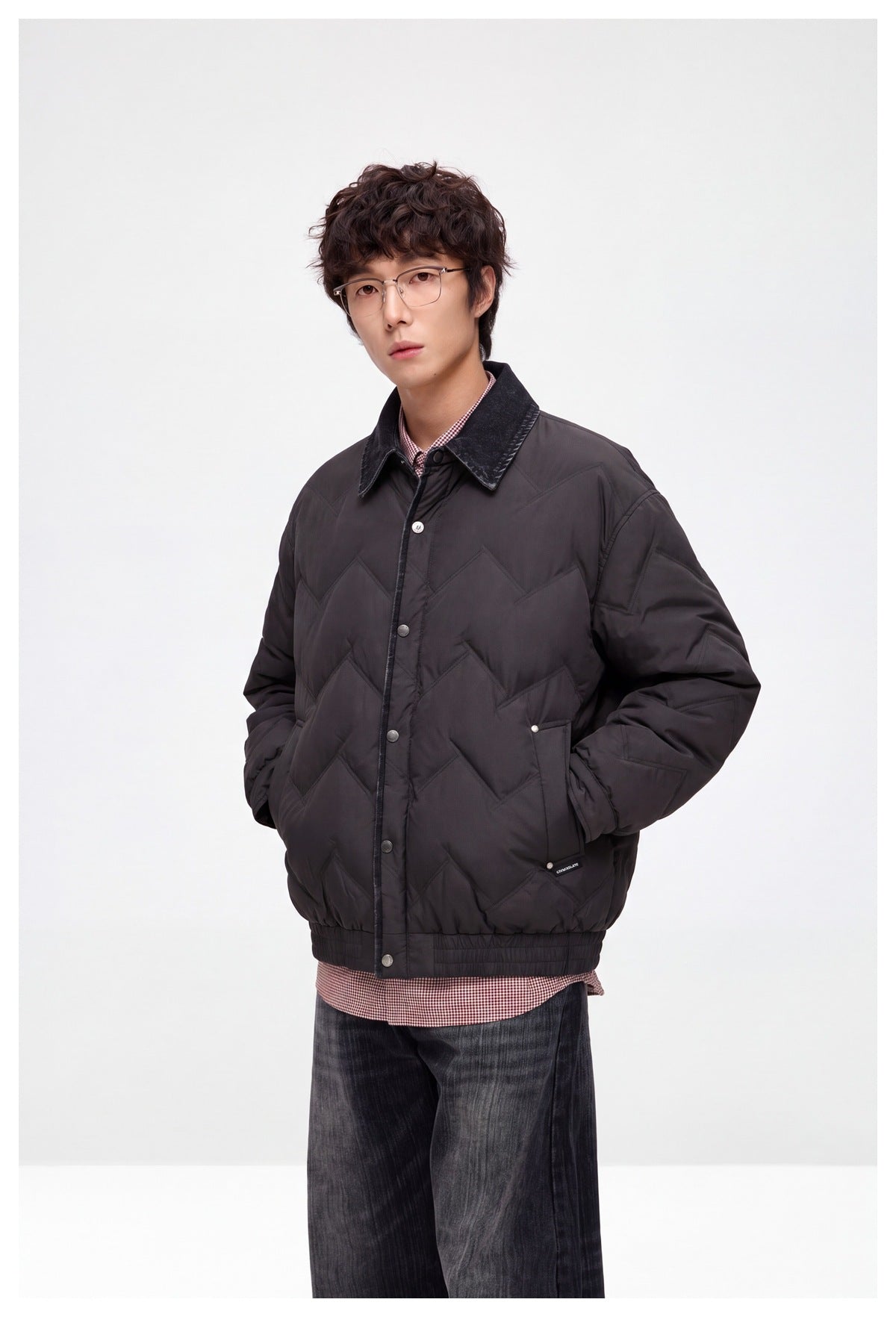 Model wearing a dark chevron-quilted jacket with a contrast collar and snap front, styled with a gingham shirt and jeans.