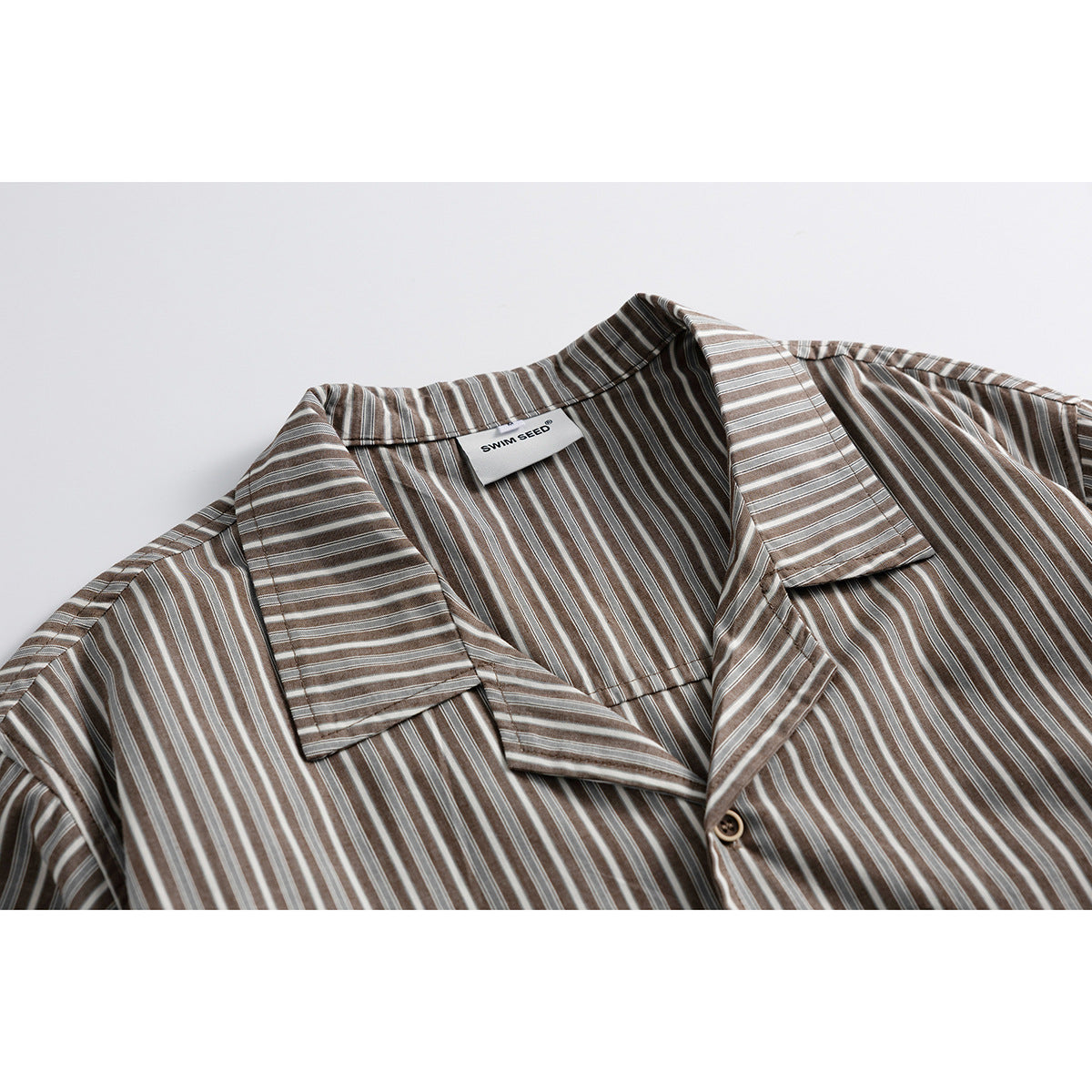 Close-up of a brown, gray and white striped short-sleeve shirt's camp collar, button and sewn-in neck label.