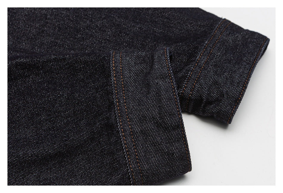 Close-up of dark indigo denim with orange topstitching along a folded edge.