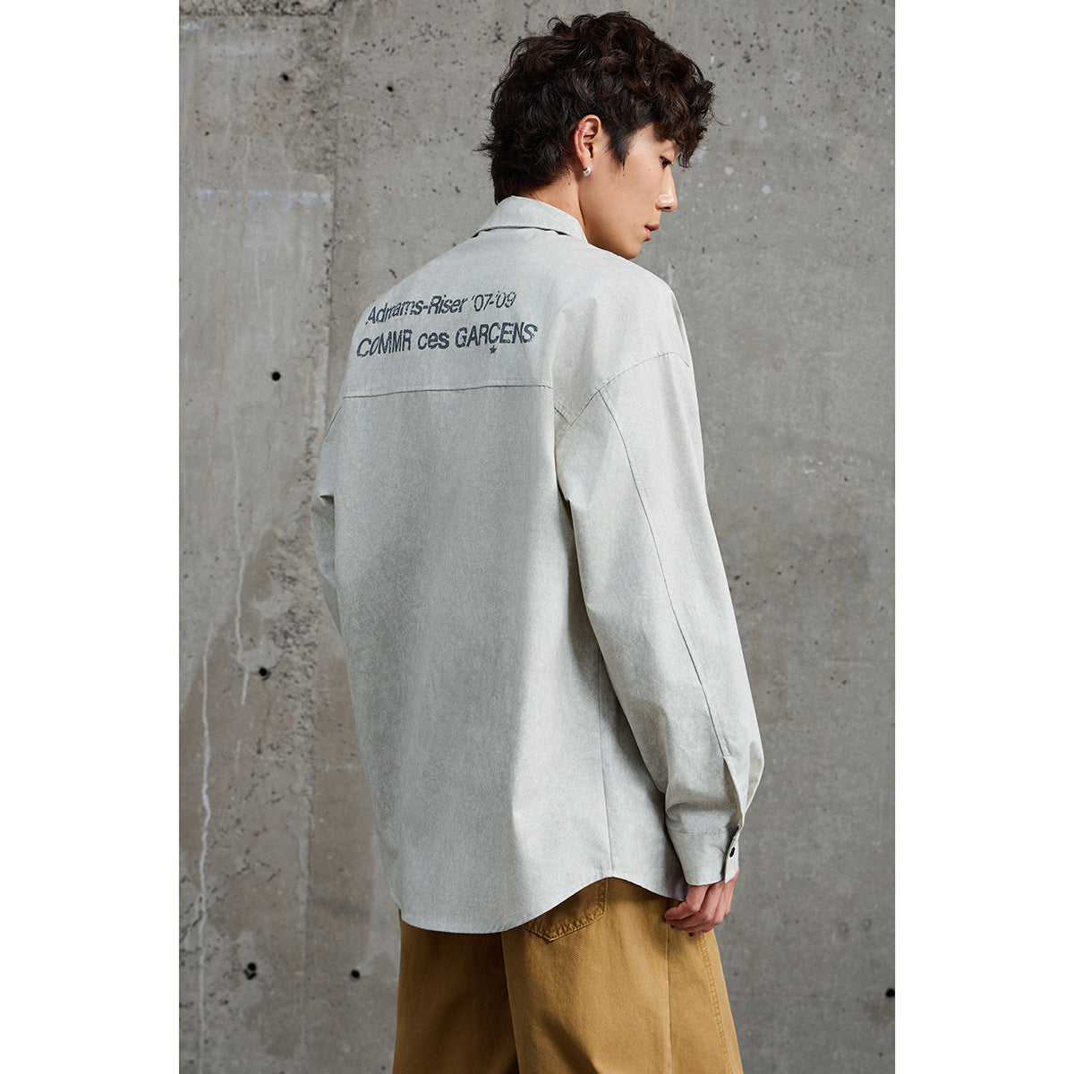 Back view of a model wearing a pale gray button-up shirt with large dark lettering across the upper back.