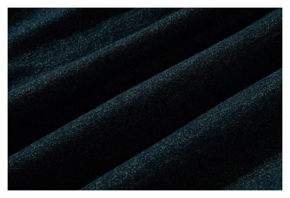 Extreme close-up of the textured dark indigo-green garment fabric in soft folds.