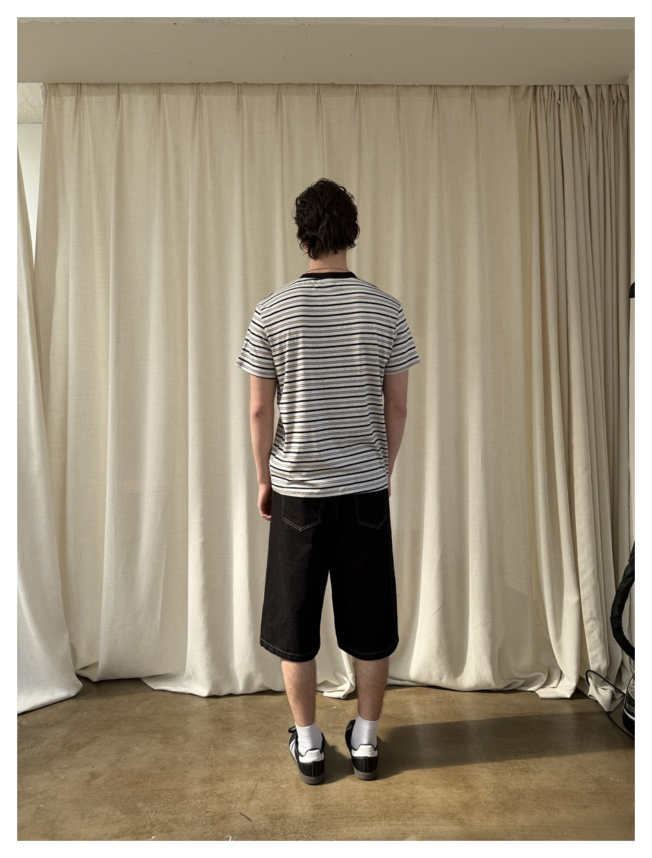 Rear view of a model wearing a white T-shirt with thin dark horizontal stripes and black shorts.