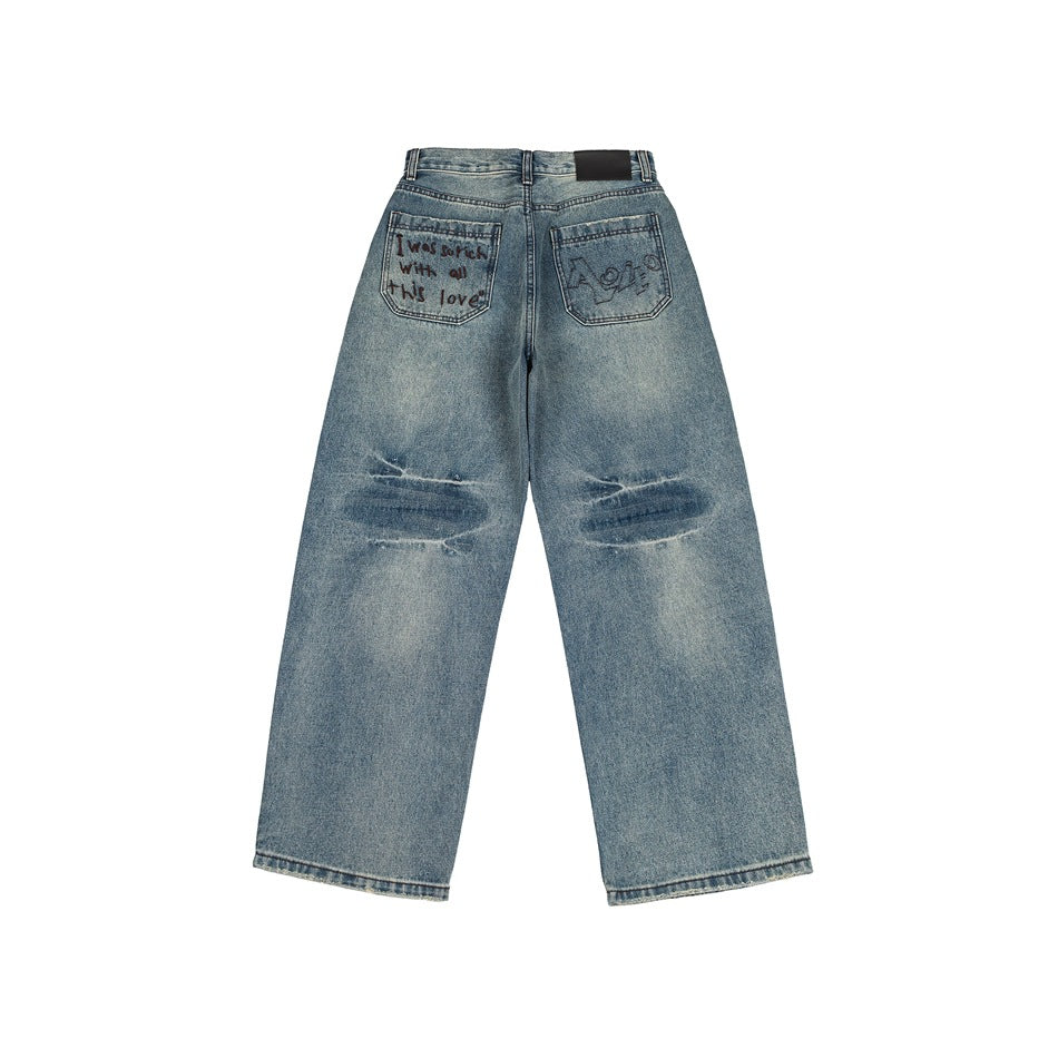 Back view of faded blue wide-leg jeans with embroidered back pockets and distressed knees, flat lay