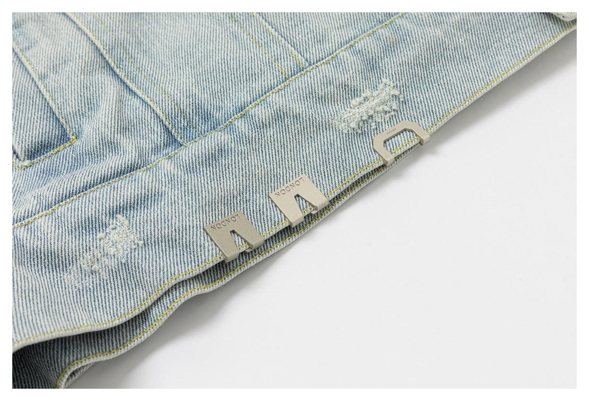 Close-up of a pale blue denim jacket hem with distressed patches and silver-tone decorative hardware.