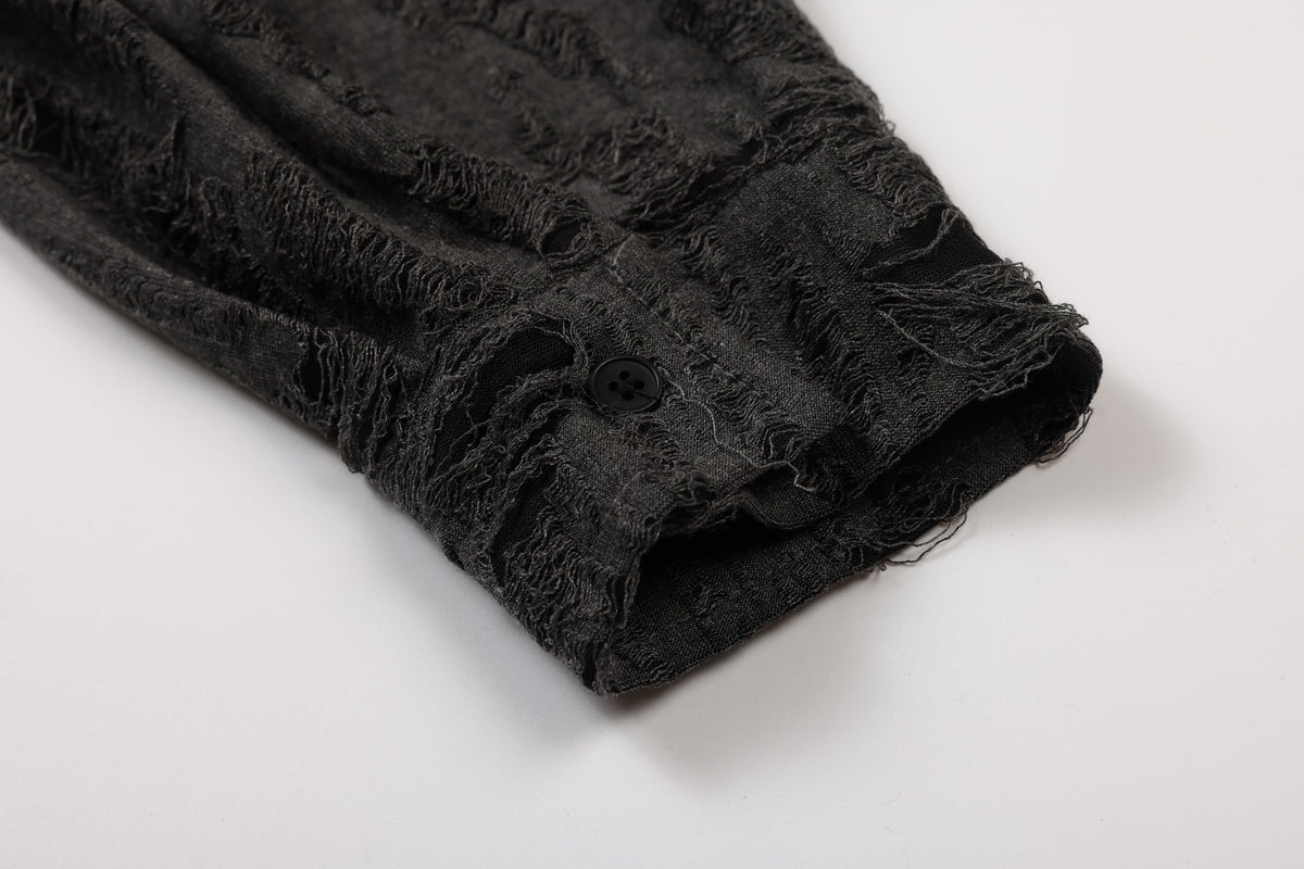 Close-up of a charcoal-black garment edge with distressed frayed texture and a black button, laid on a white surface.