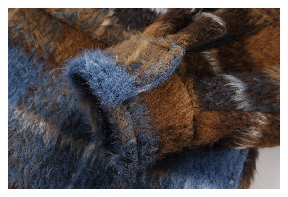 Close-up of a plaid jacket cuff with a dark fastening tab and fuzzy blue and brown fabric.