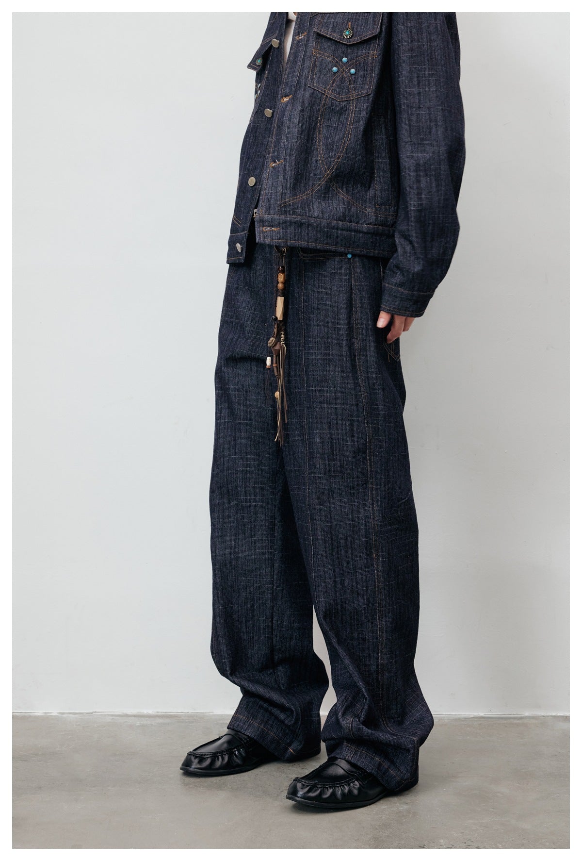 Model wearing dark indigo wide-leg jeans with matching denim jacket, key charm and black loafers, side view