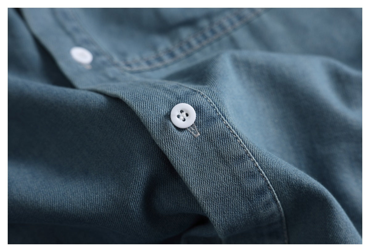 Close-up of a blue denim shirt placket with white buttons and visible stitching.