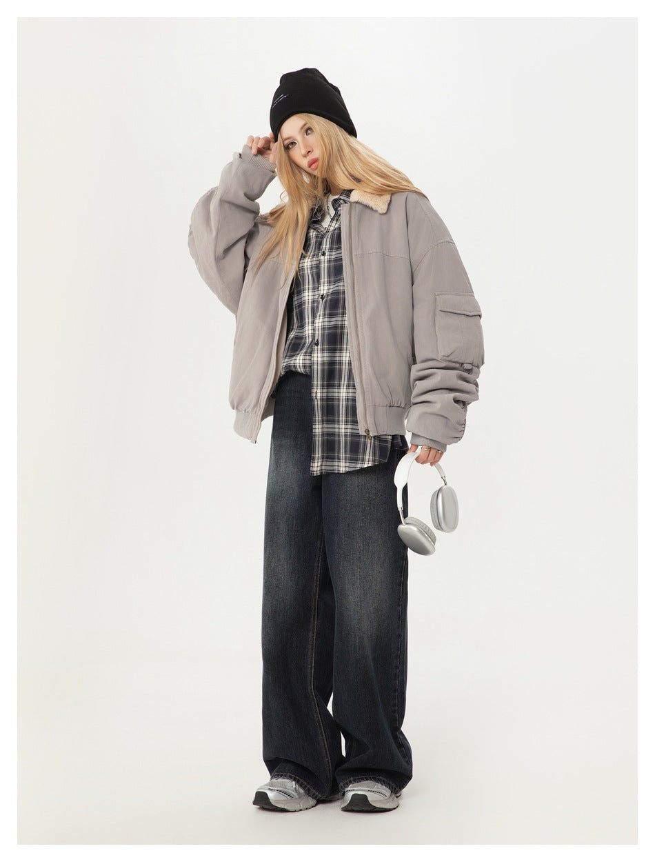 Model wearing a light gray bomber jacket with a cream shearling collar, plaid shirt, and dark jeans.