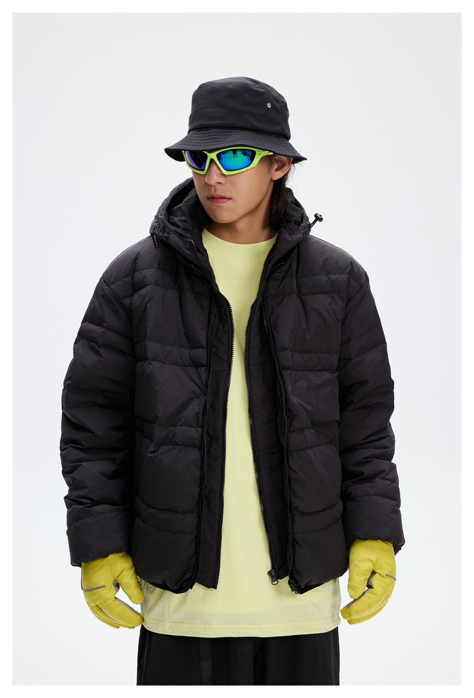 Front view of a model wearing an open black hooded puffer jacket over a pale yellow shirt.
