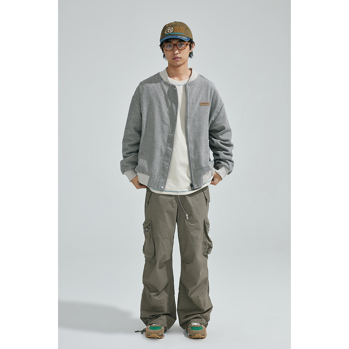 Full-length front view of a model wearing a gray herringbone bomber jacket and loose olive cargo pants.