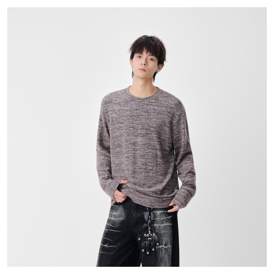 Model wearing a loose, mottled taupe-gray crewneck sweater with long sleeves and black jeans.