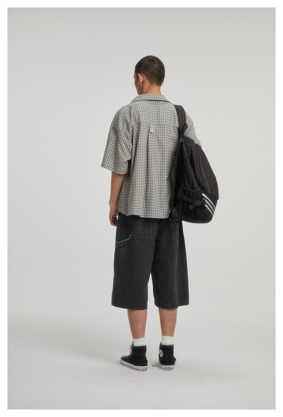 Back view of a model wearing a gray plaid short-sleeve shirt and black knee-length shorts, with a black backpack.