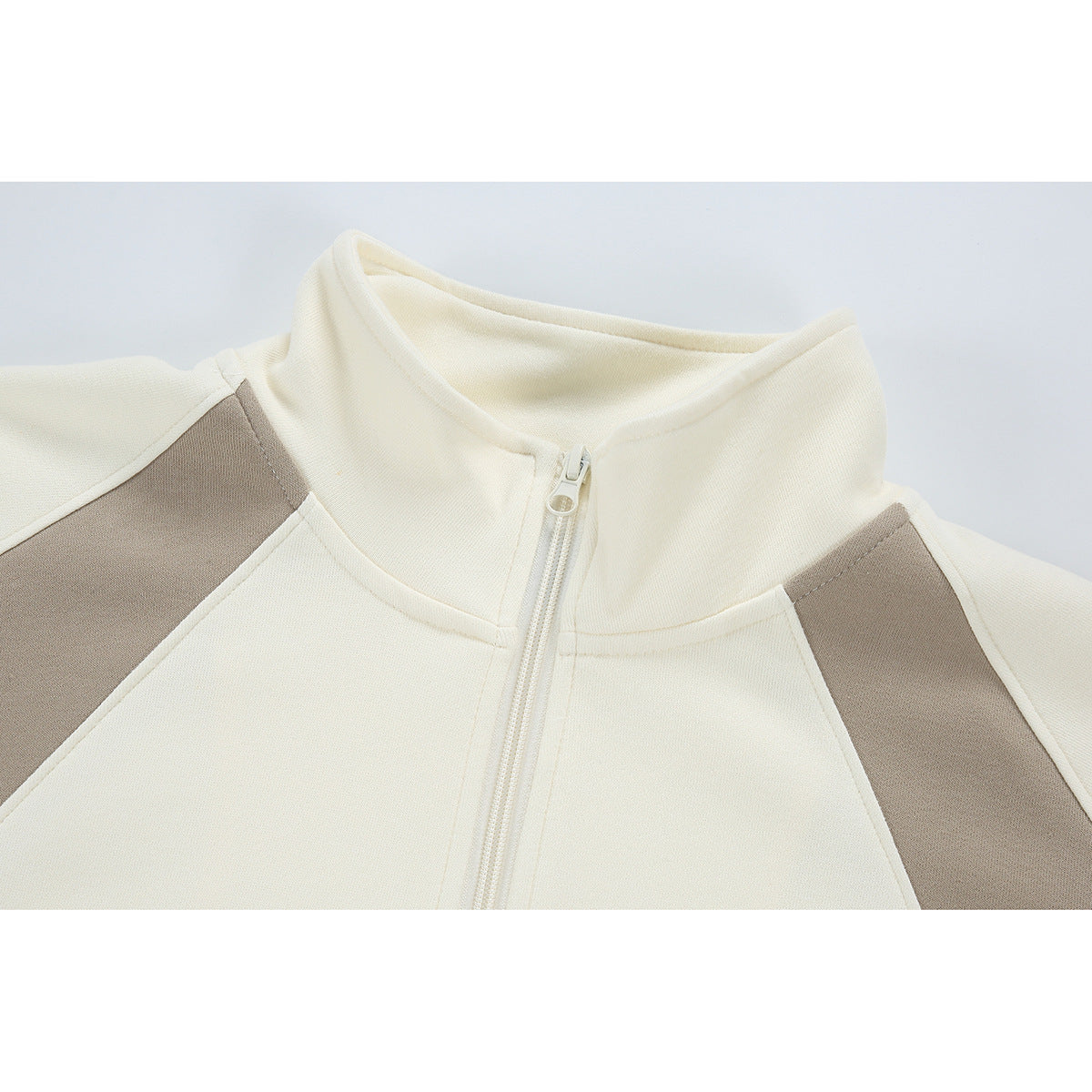Close-up of an ivory zip-up jacket with a stand collar and taupe shoulder panels.