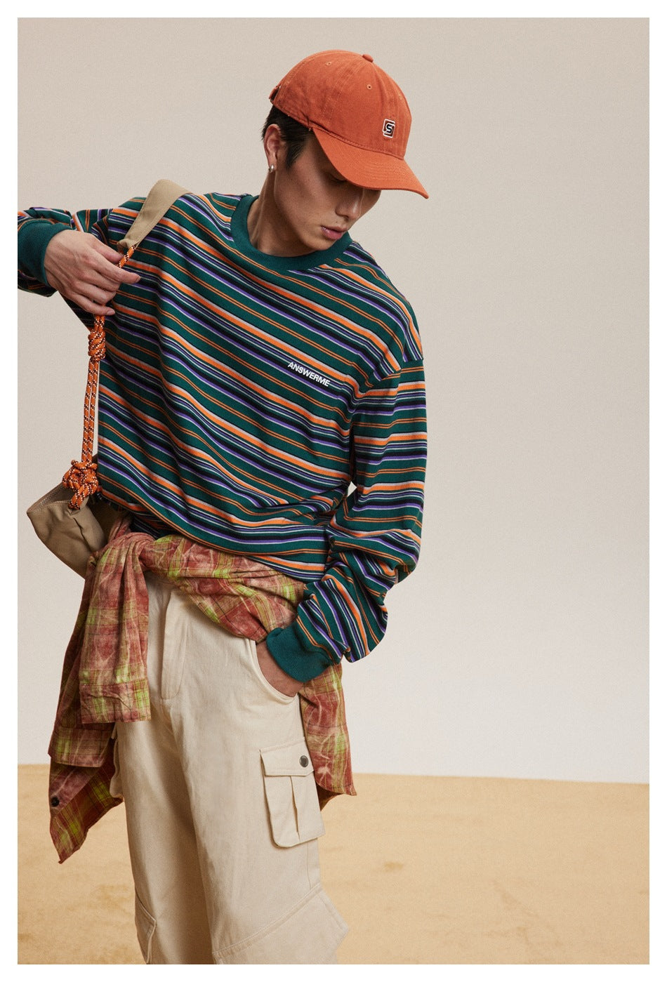 Model wearing a teal, orange, purple and white striped long-sleeve shirt with beige cargo pants and an orange cap.