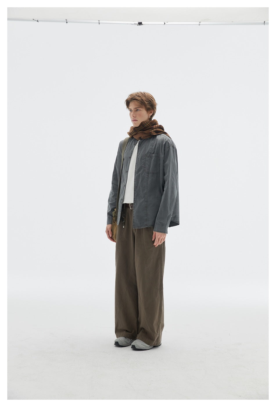 Model standing in side view wearing brown wide-leg pants with a gray shirt, plaid scarf and sneakers