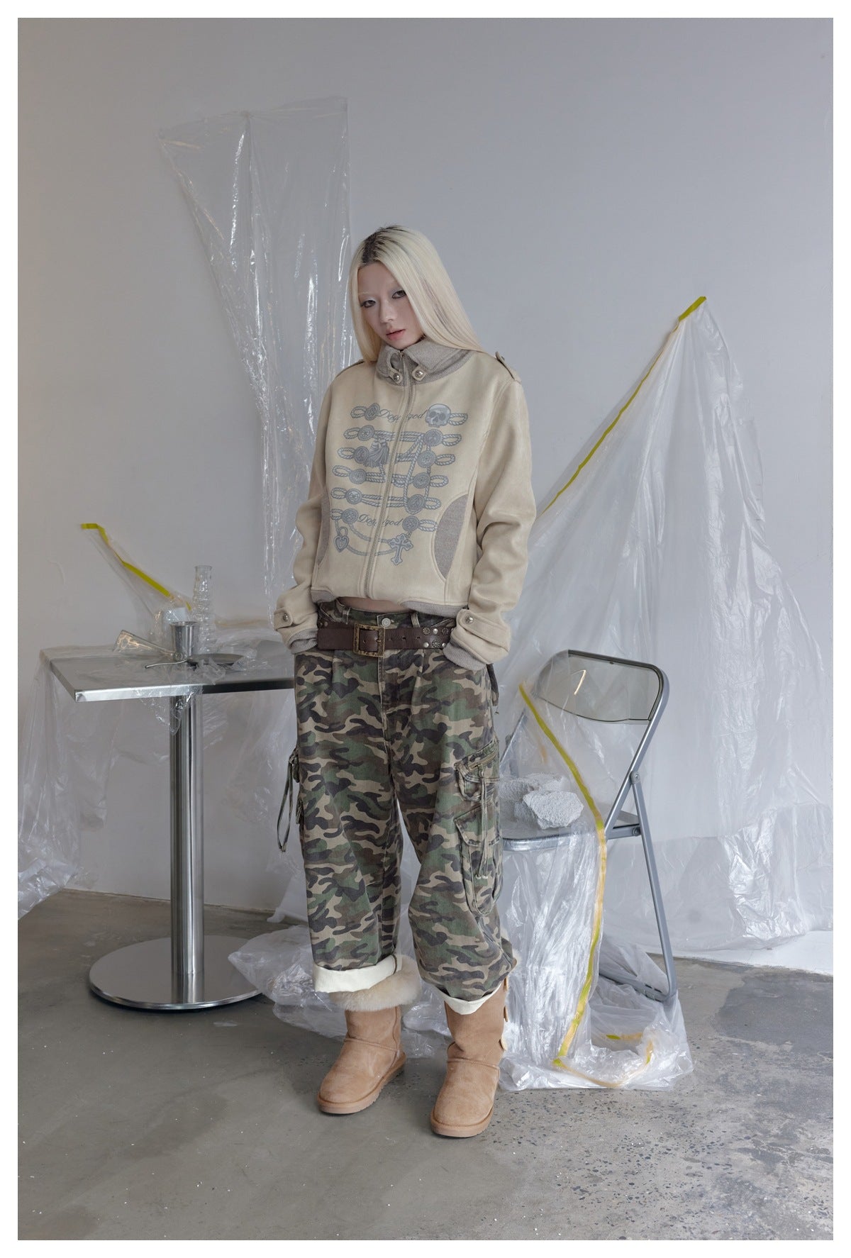 Model wearing the beige cropped zip jacket with camo cargo pants, brown belt and tan boots, standing in a studio