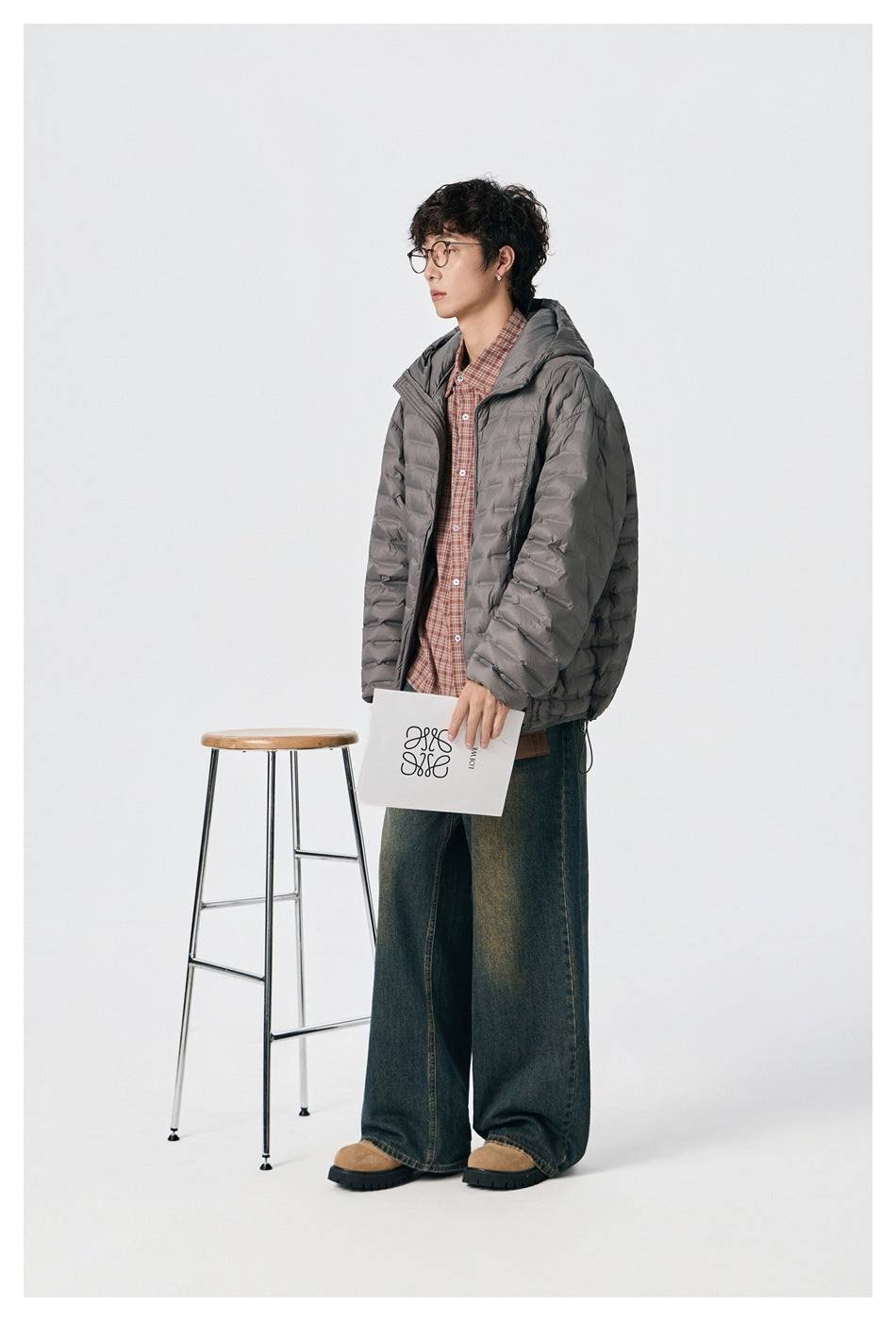 Side view of a model wearing an open gray quilted hooded jacket over a plaid shirt.