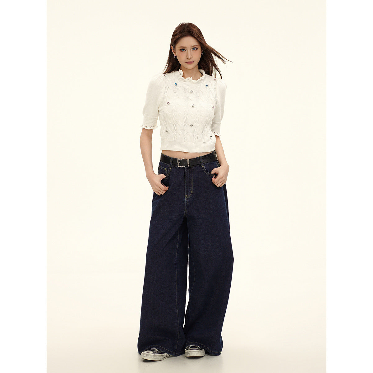 Full-length front view of a model wearing an ivory embellished knit top, dark wide-leg jeans, and a black belt.