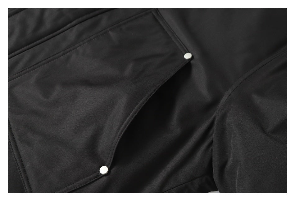 Close-up of a black jacket pocket with angled edges and silver snap buttons.