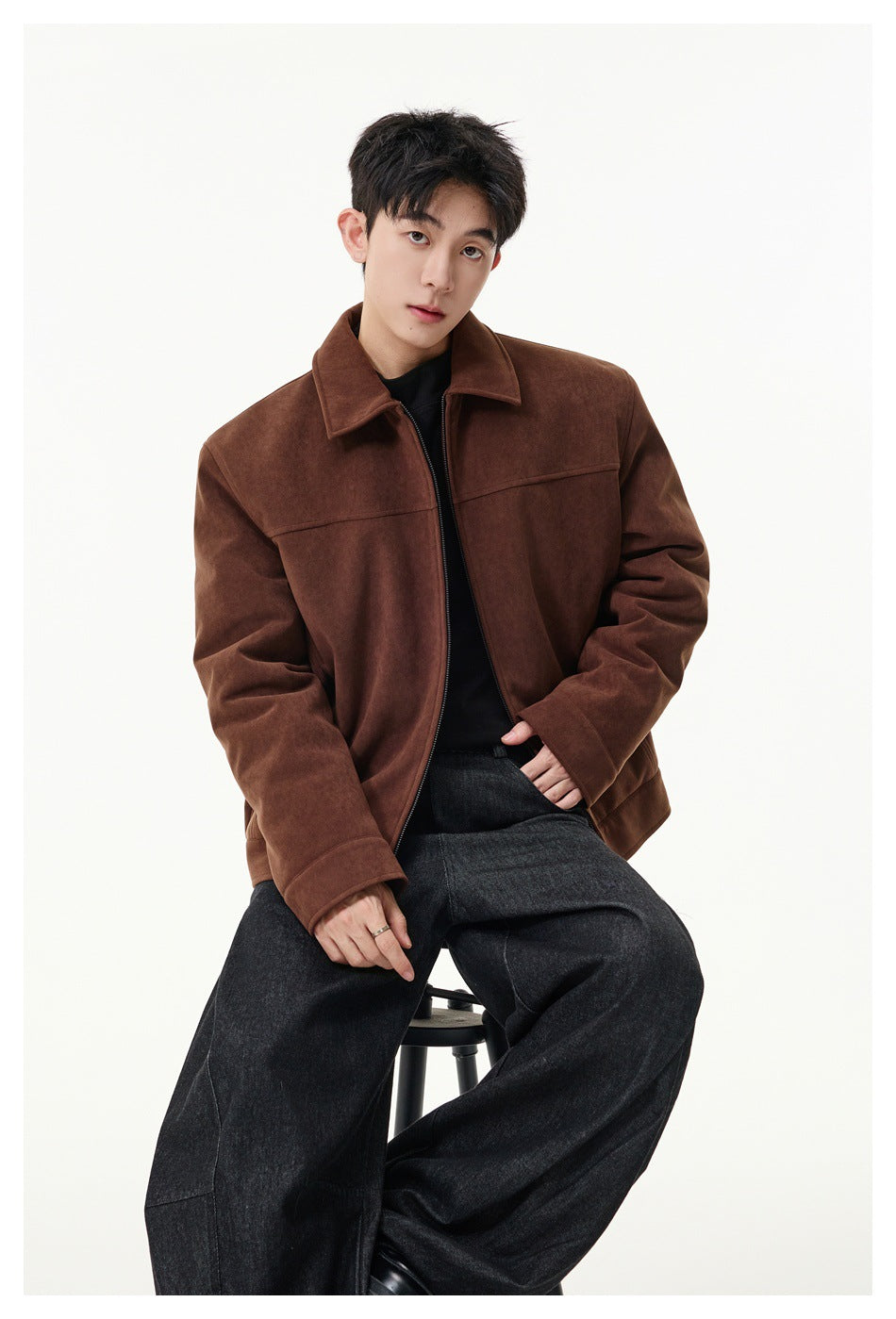 Seated model wearing a brown collared zip jacket over a black top with dark wide-leg jeans.