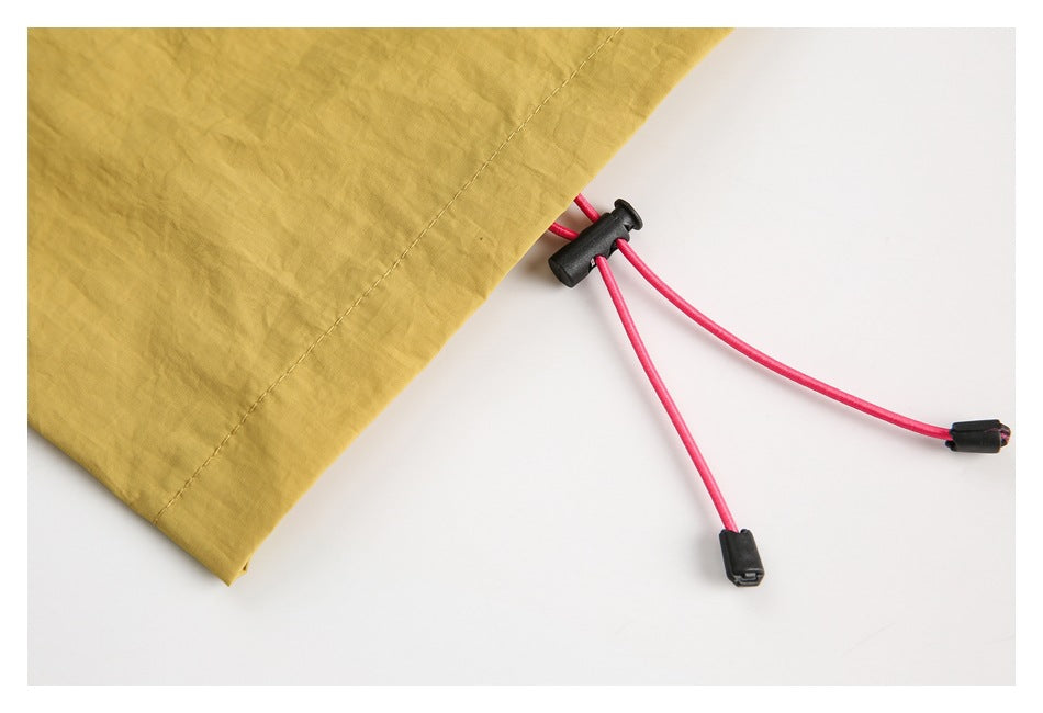Close-up of mustard-yellow garment hem with bright pink drawcords and black cord locks.