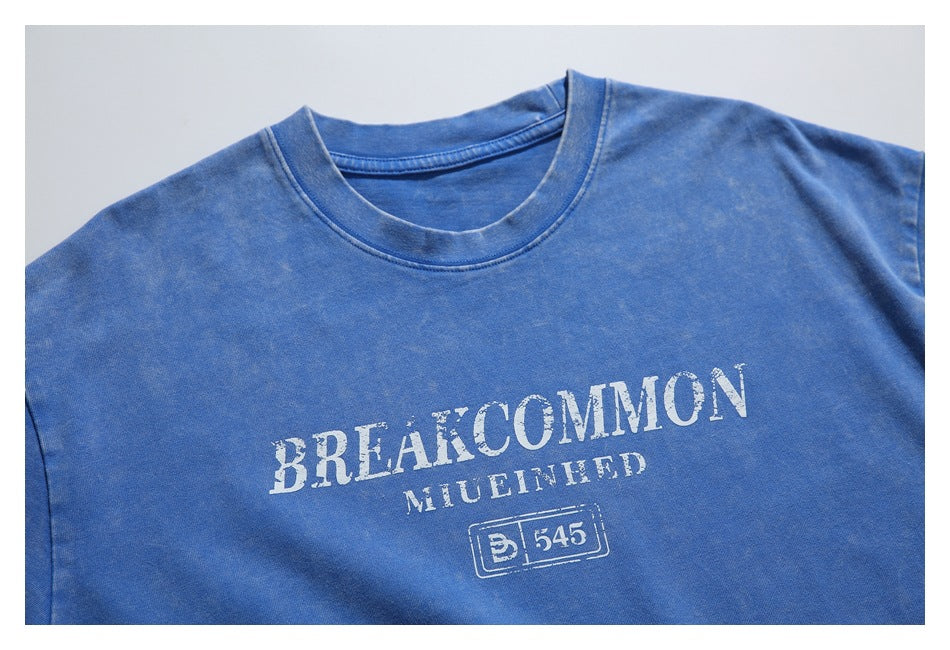 Close-up of the blue T-shirt's crew neckline and distressed white chest lettering with a boxed emblem.