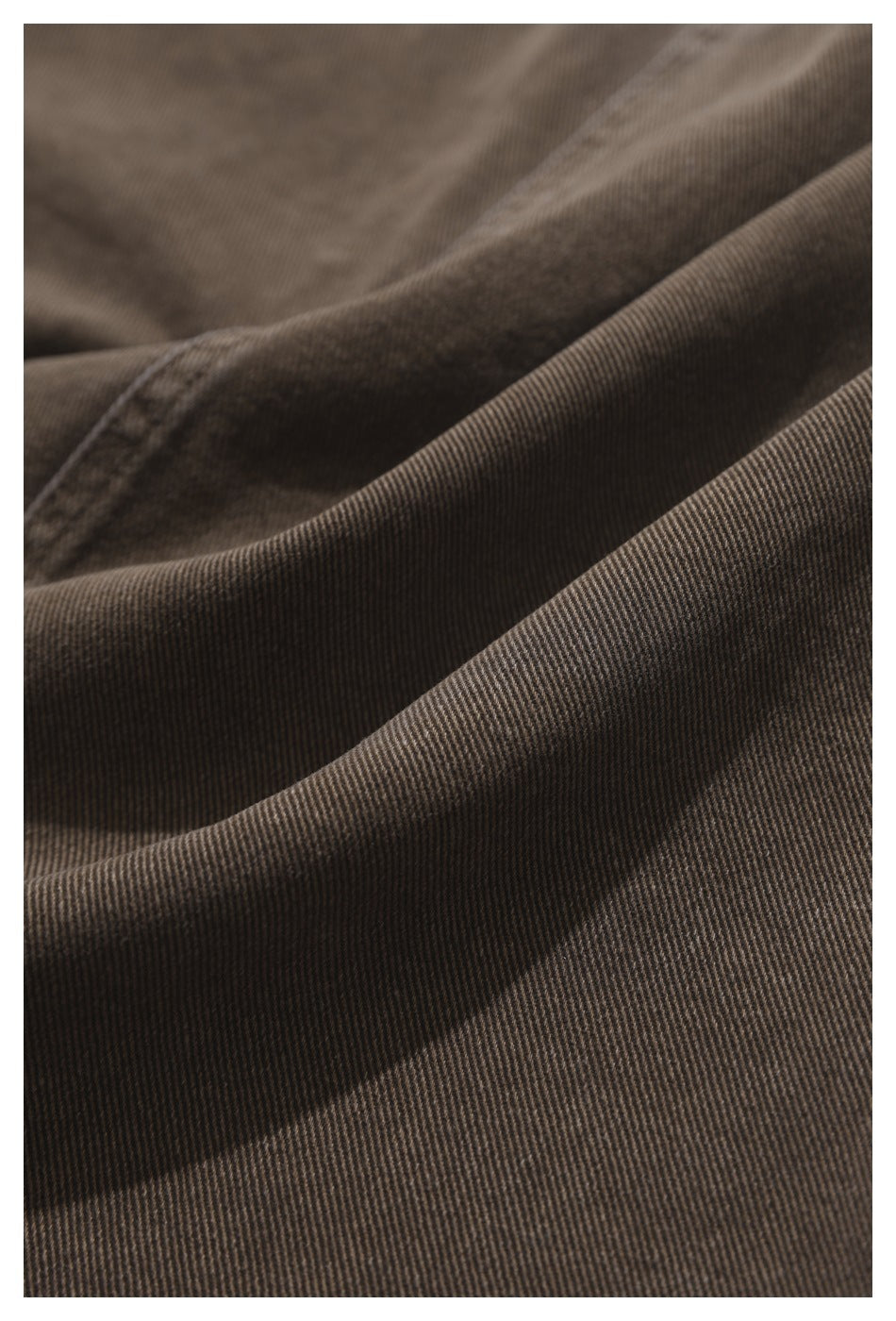 Close-up of brown-gray garment fabric draped in folds, highlighting its fine diagonal weave.