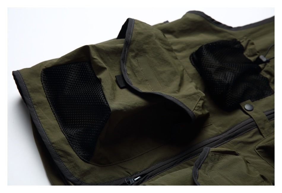 Close-up of an olive vest flap pocket and black mesh panel, with dark edging and zipper visible.