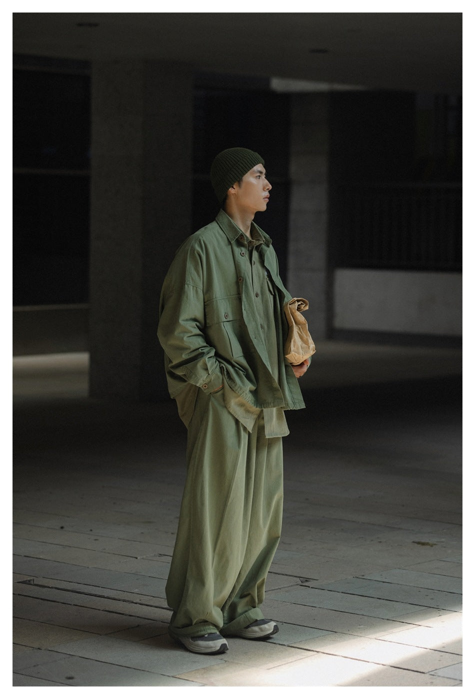 Model in a sage green oversized button-up jacket with flap pockets and loose matching trousers, shown in profile.