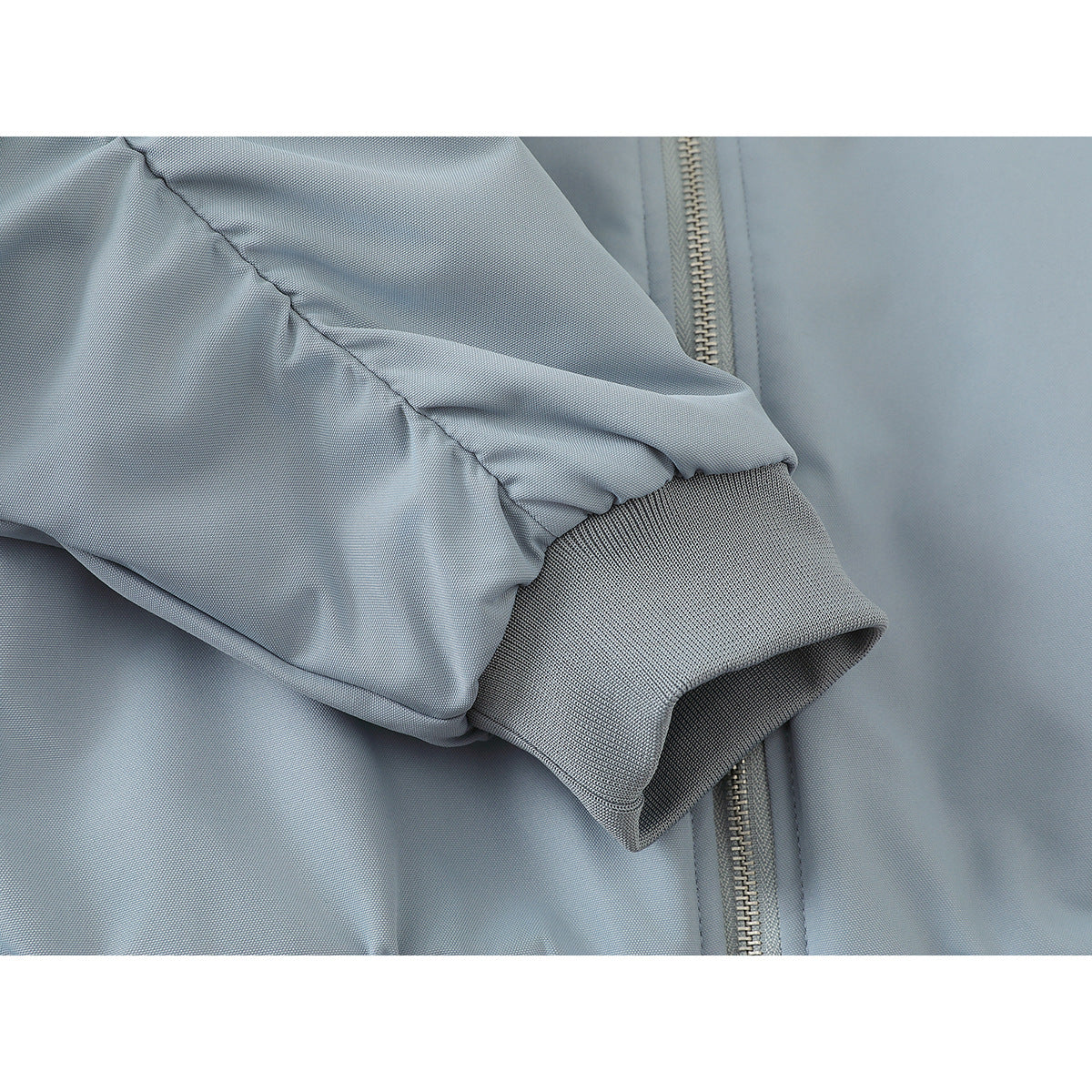 Close-up of a pale blue jacket sleeve with a ribbed gray cuff beside the front zipper.